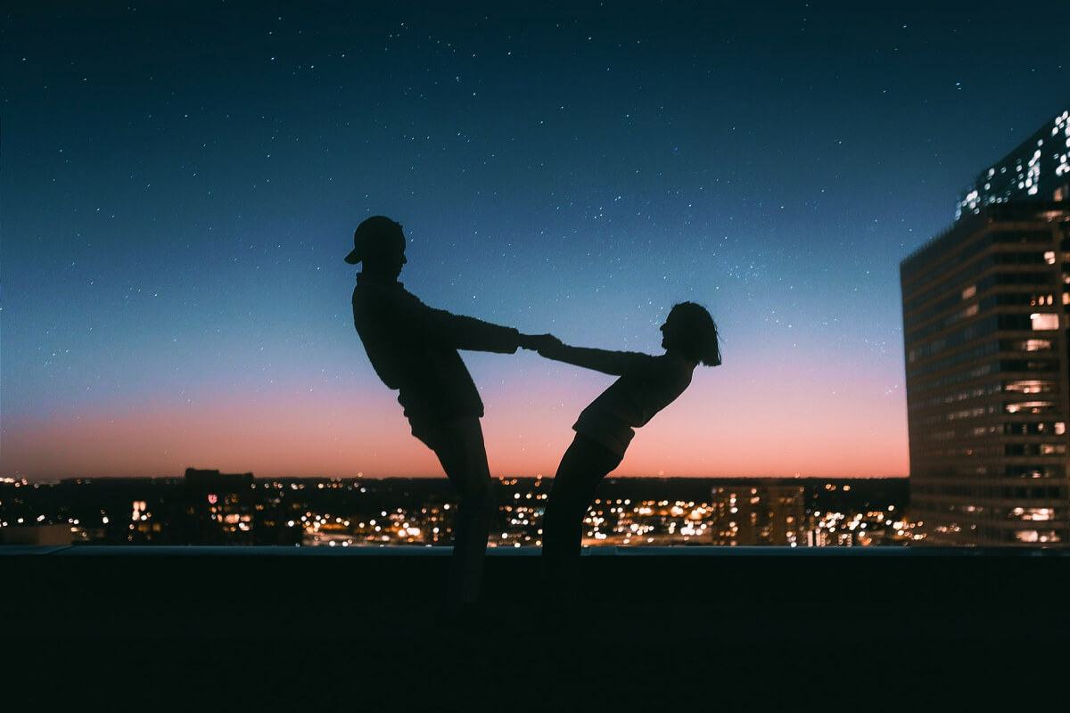 A couple in love, holding hands, silhouetted in front of a city skyline at sunset