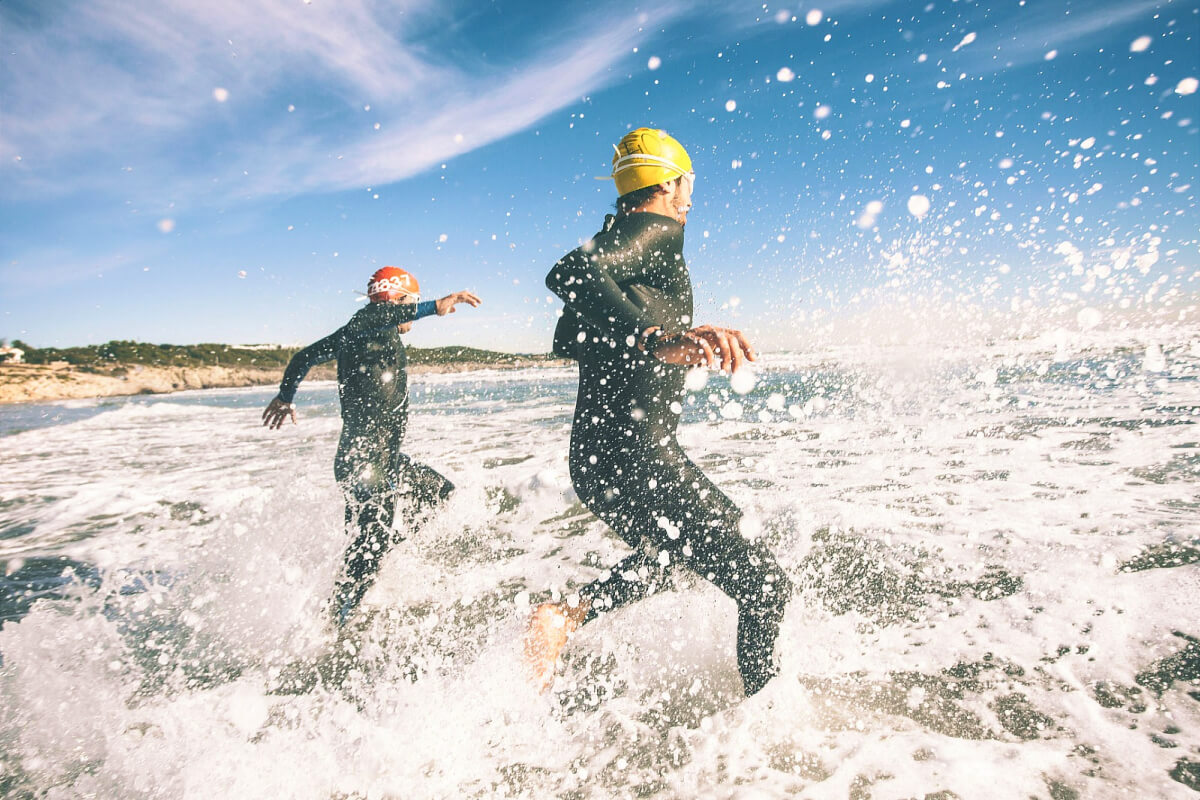people running in the ocean in wet suits