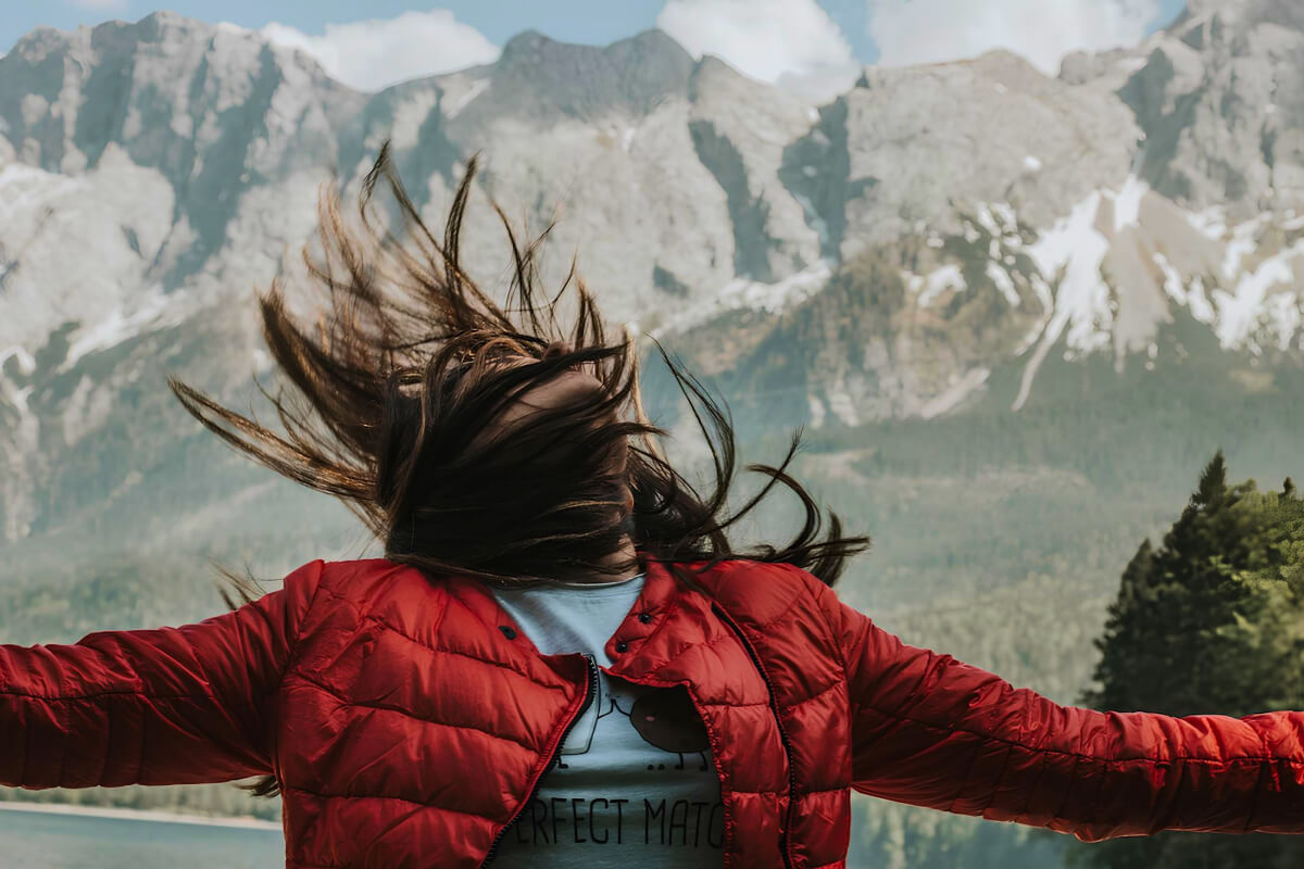 woman in red wind breaker jacket looking up hair blowing