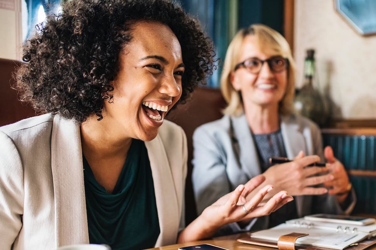 African American female and blonde Caucasian coworker laughing during at table
