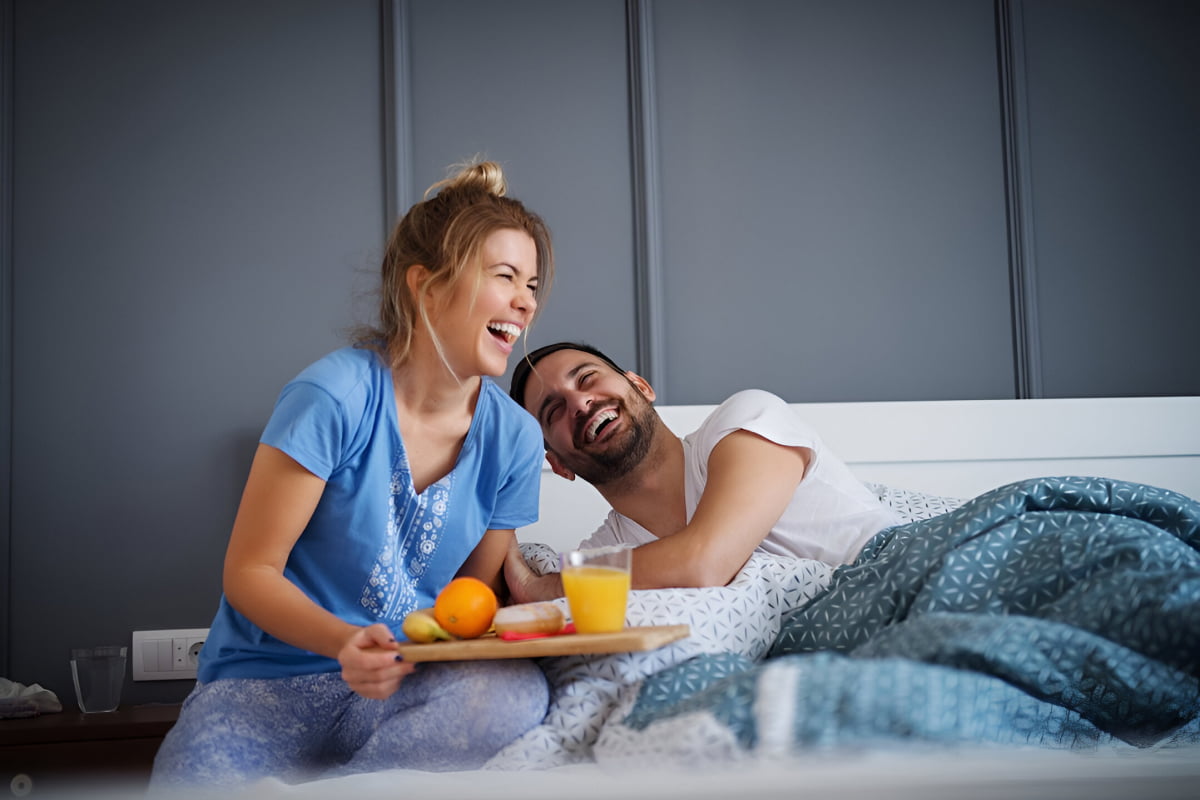 man and woman laughing with breakfast in bed