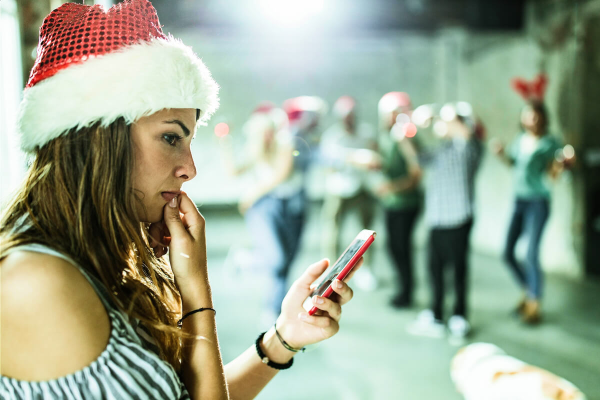 Woman looking at phone wearing Santa hat at office holiday party