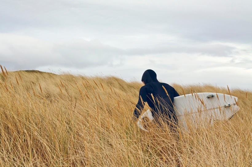 man walking through a field with a surfboard