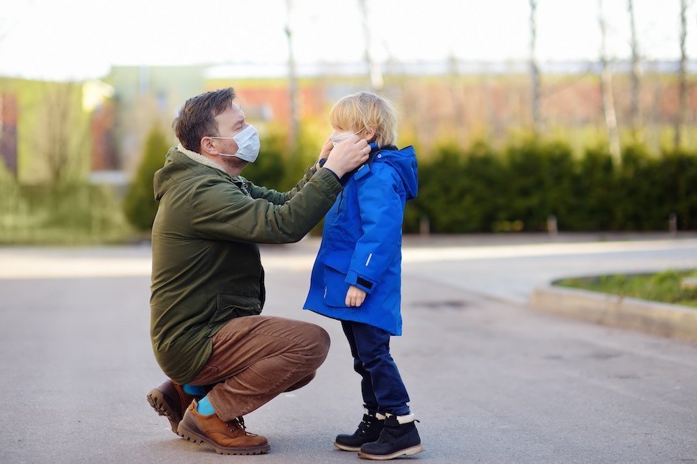 Father kneeling down putting on sons facemask