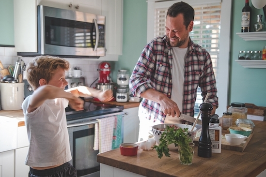 Father and son laughing while cooking in a kitchen