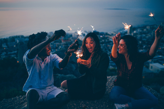 Three people sitting outside holding sparklers and laughing