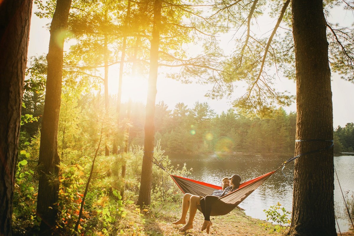 Woman and man sitting in a hammock next to a river