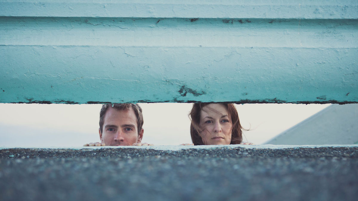 Woman and man looking through a gap in wall outside