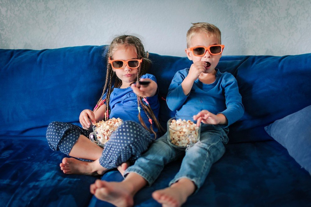 kids eating popcorn on a couch wearing 3d glasses watching a movie