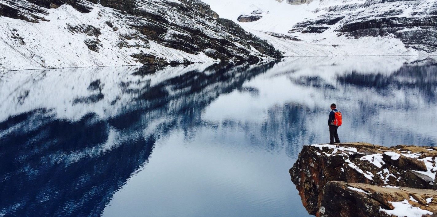 Man standing on cliff looking as clear water and mountains