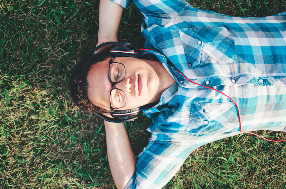Man laying on grass with eyes closed and headphone on