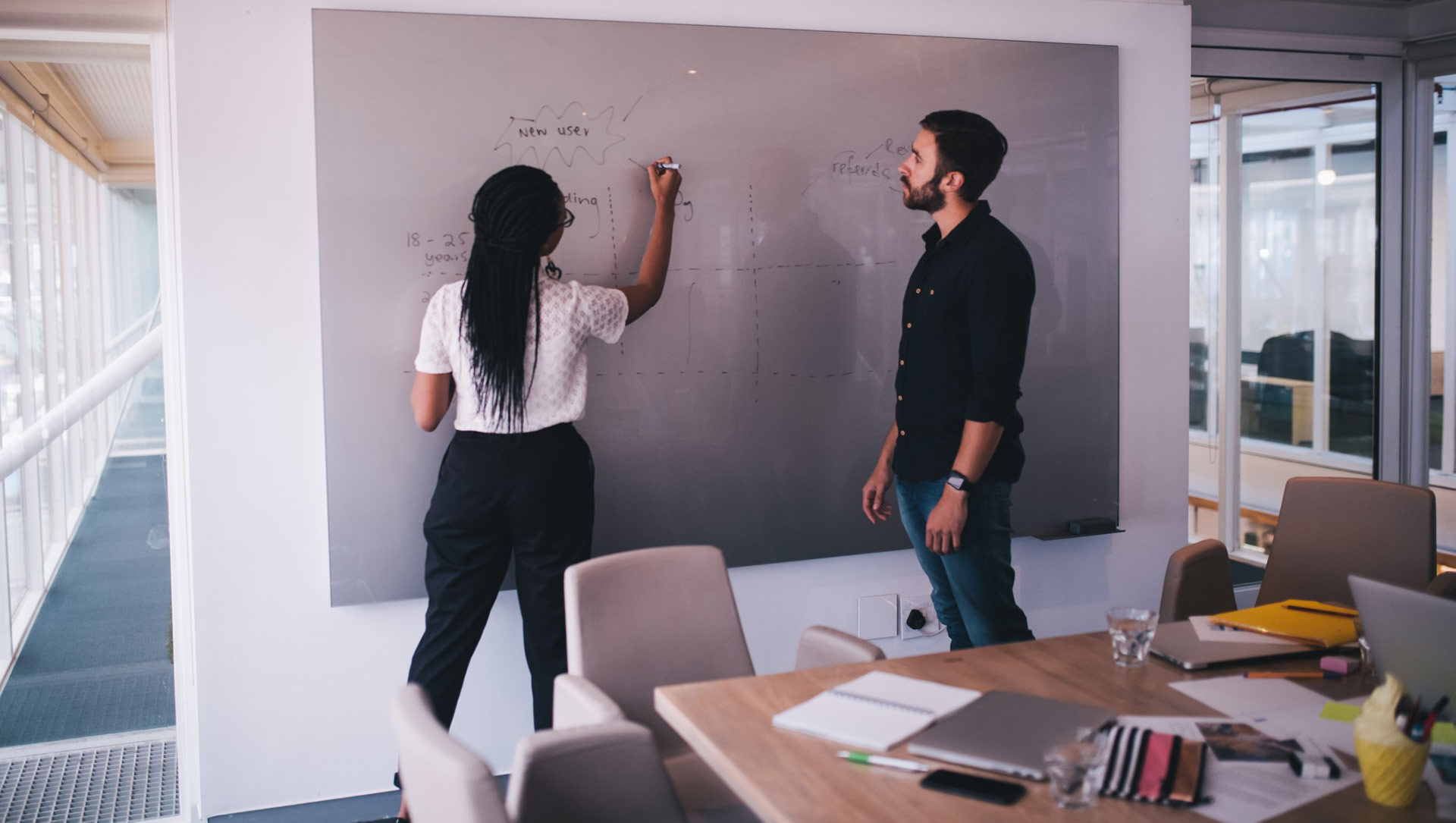 Woman writing on whiteboard with man watching in the office