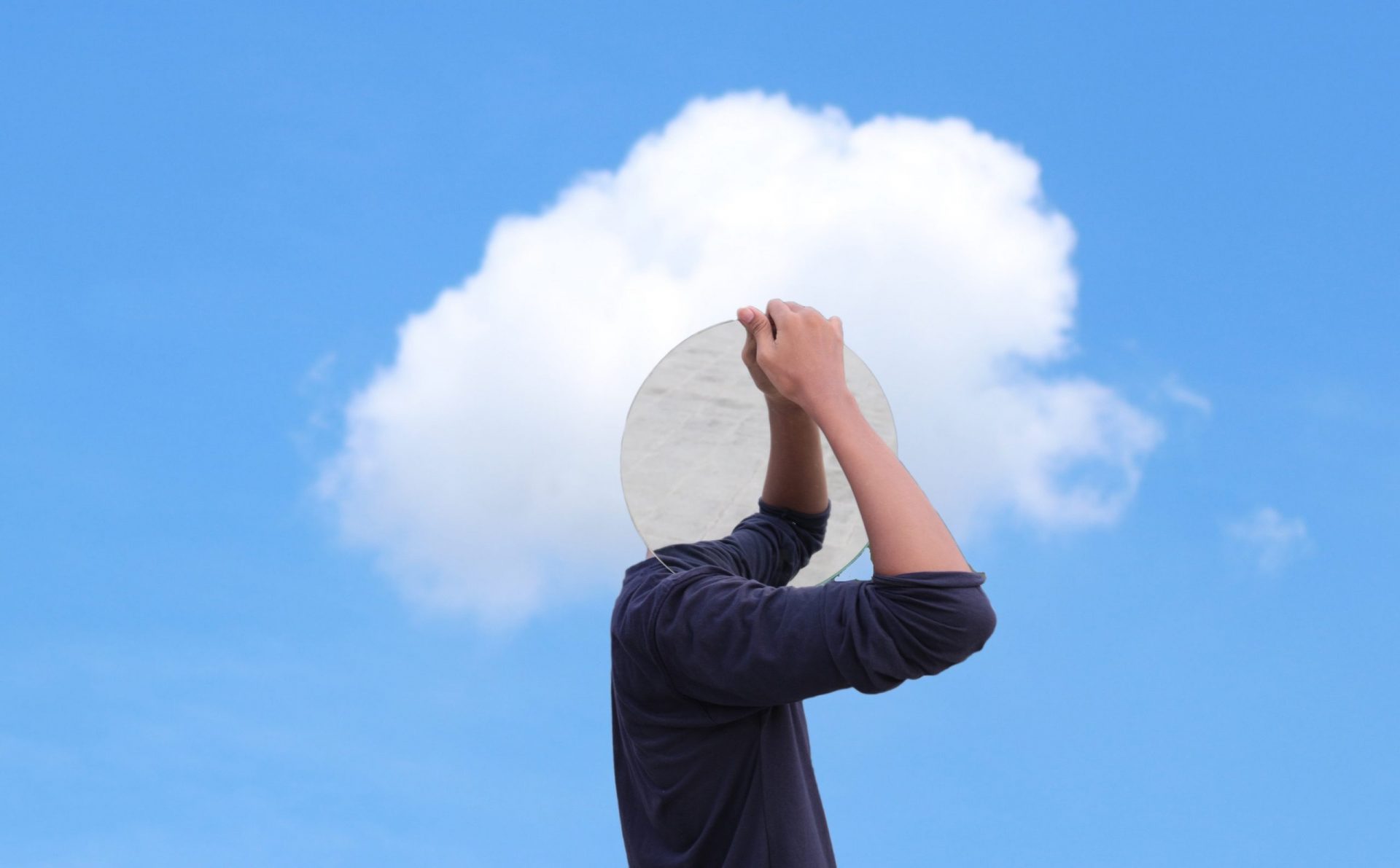 Man covering head with a mirror blue sky background