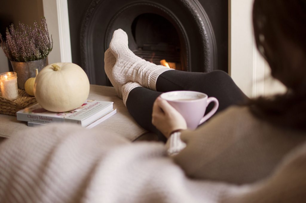 A woman sits with her feet up next to a fire the atmosphere is cosy and the socks are wooly