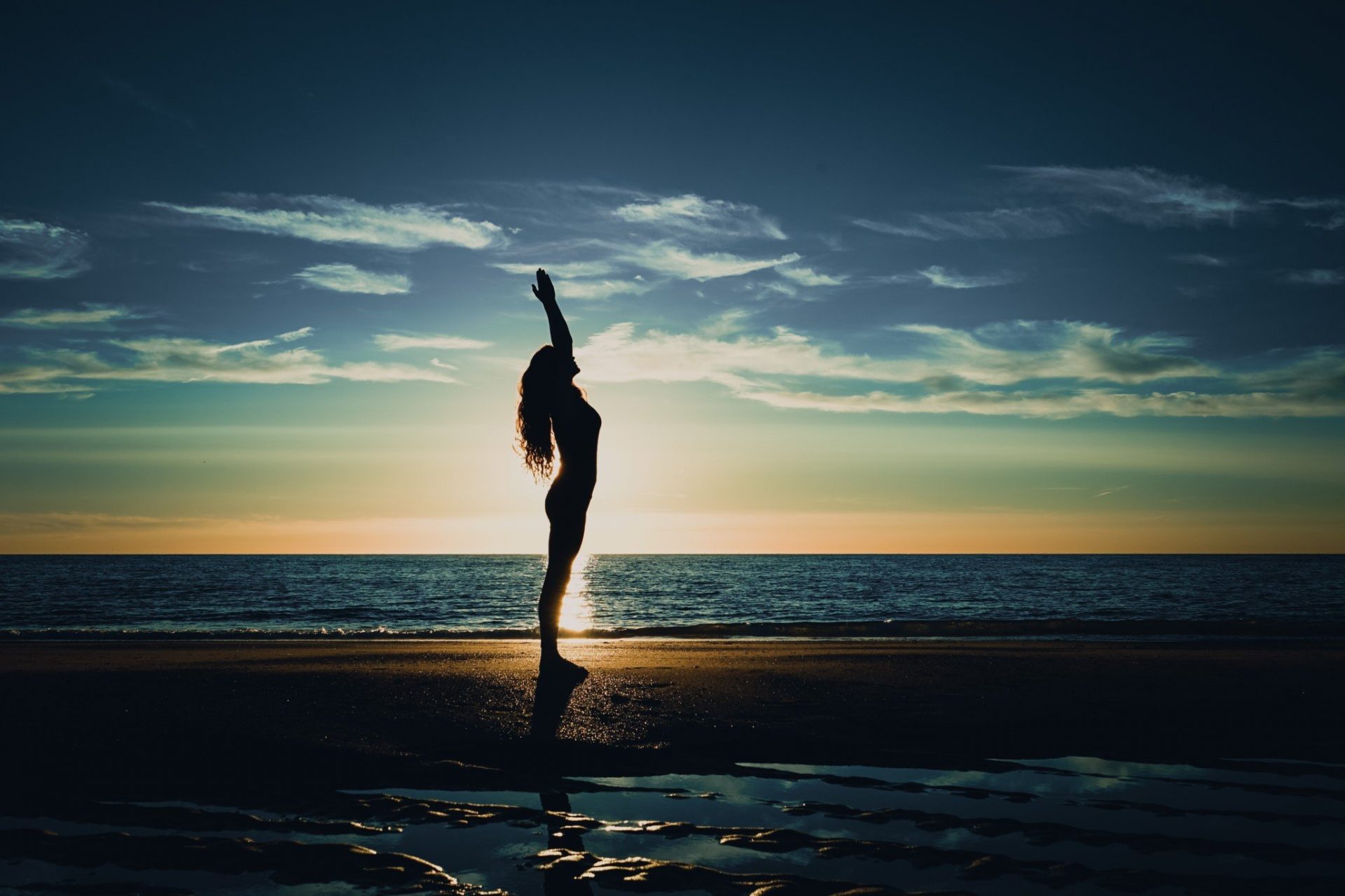 A woman is doing yoga during the sunset on the beach