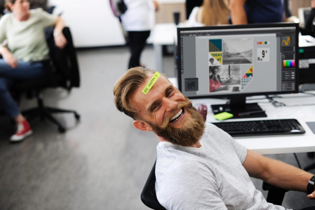 Employee smiling in office with a be happy note on his forehead