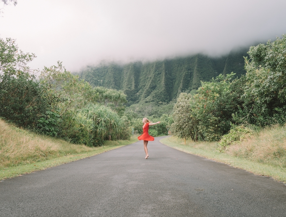 Woman dancing in the middle of an empty road surrounded by trees