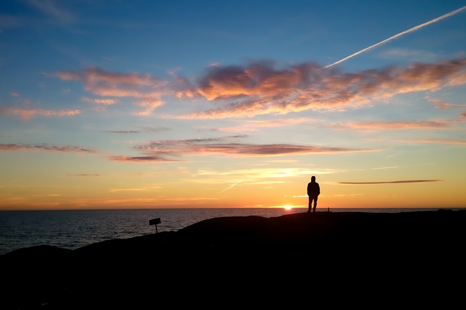 lonely person standing on rocks at sea looking at sunset