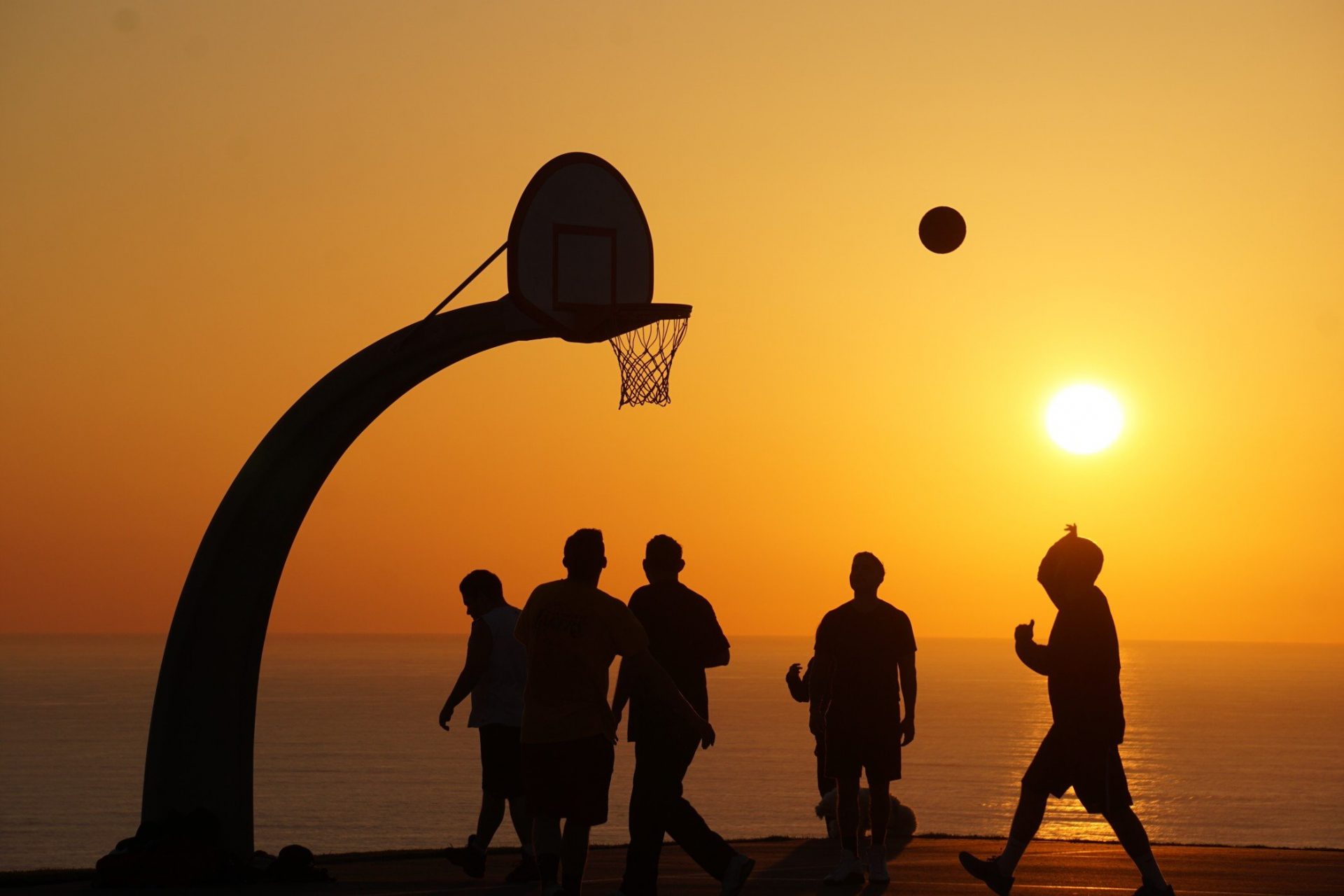 people playing basketball on the beach during sunset