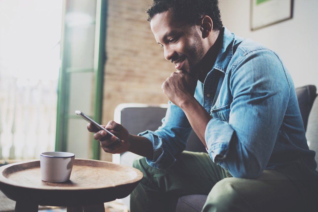 African American man smiling at his phone with coffee