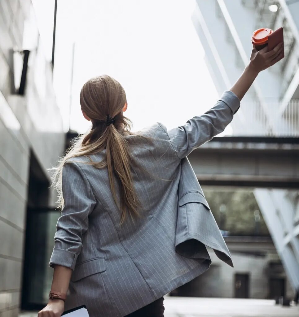 Back view of professional woman holding up arm while holding coffee cup and mobile phone