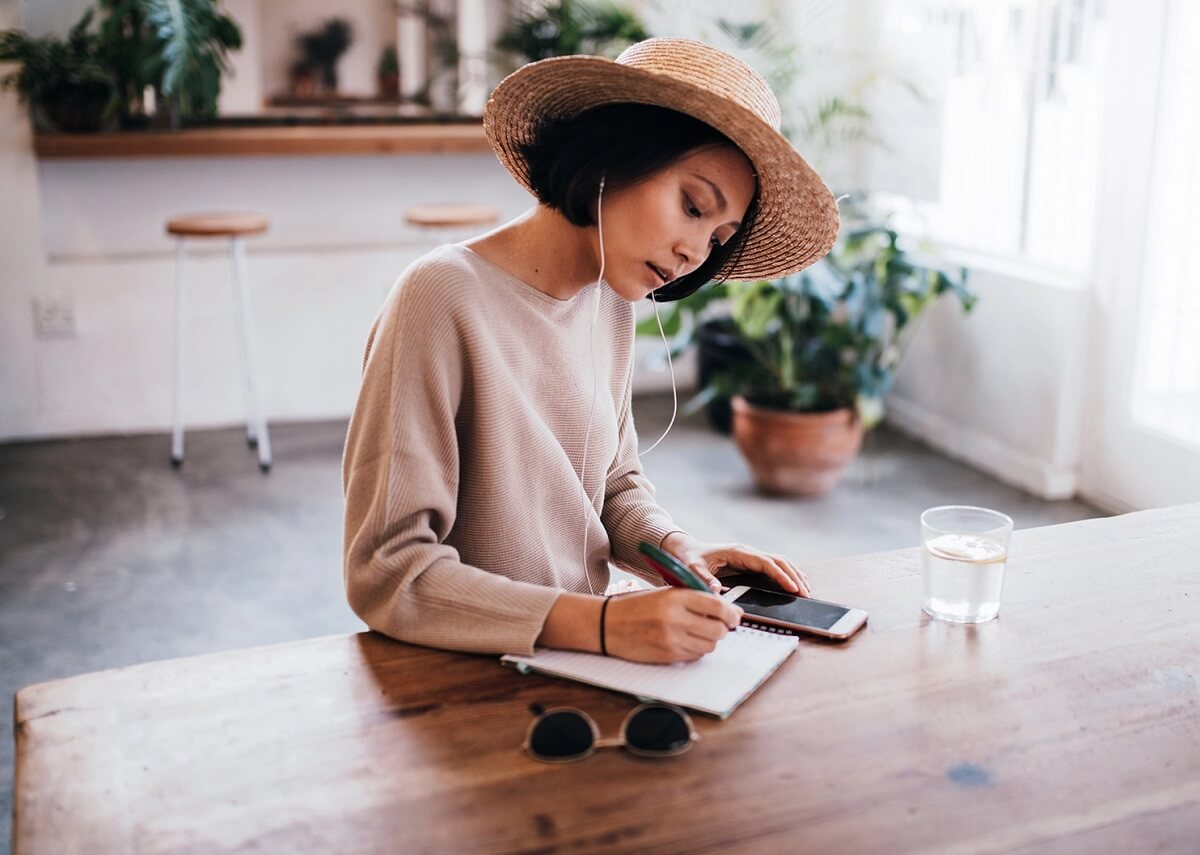 Woman sitting down with headphones in and writing in a notepad