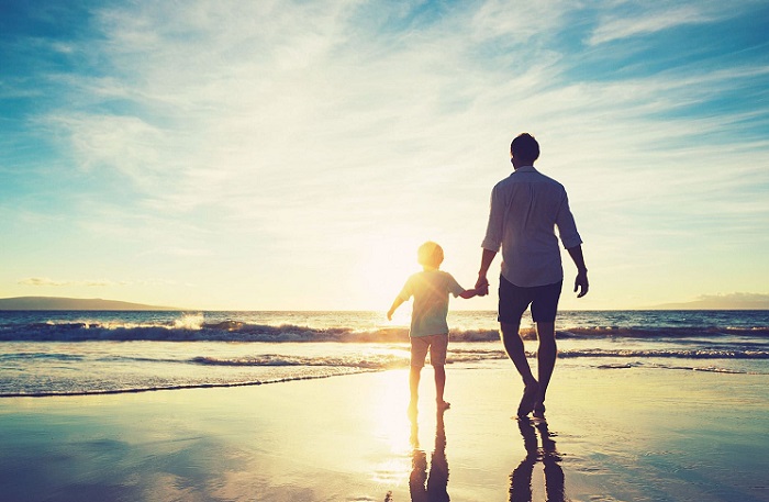Father and sun walking along beach at sunrise