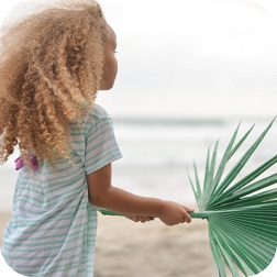 Young girl on beach holding palm leaf