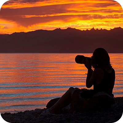 Woman photographer taking pictures of lake at sunset