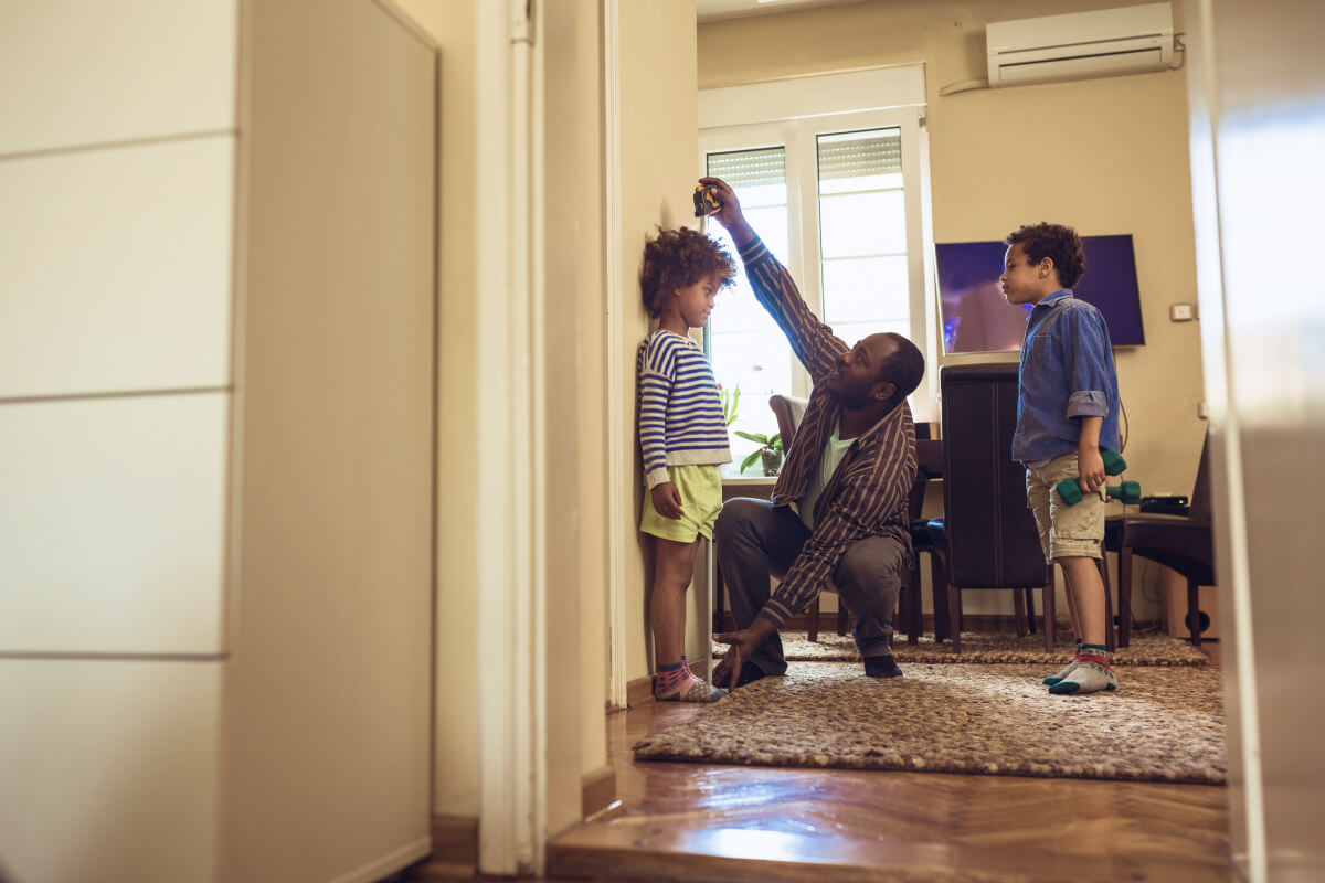 African American father checking height of his two children on wall with tape measure