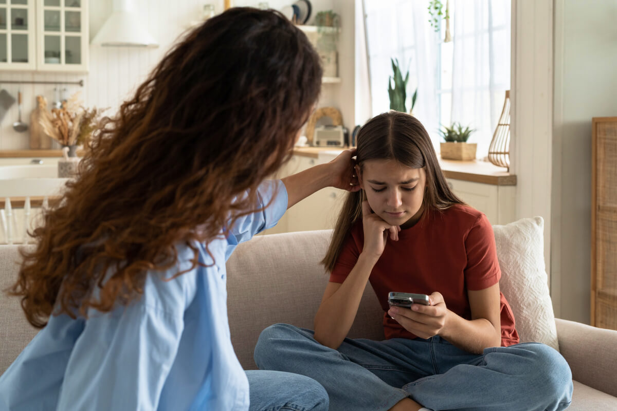 supportive mother comforting sad teenage daughter, who is being bullied, on living room couch