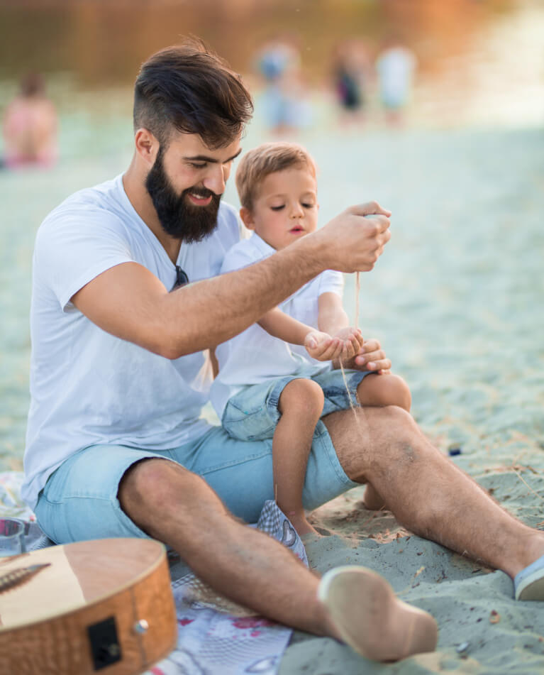 Father and neurodiverse son playing with sand on beach