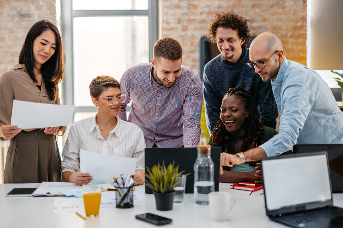 Diverse group of office employees looking at same laptop