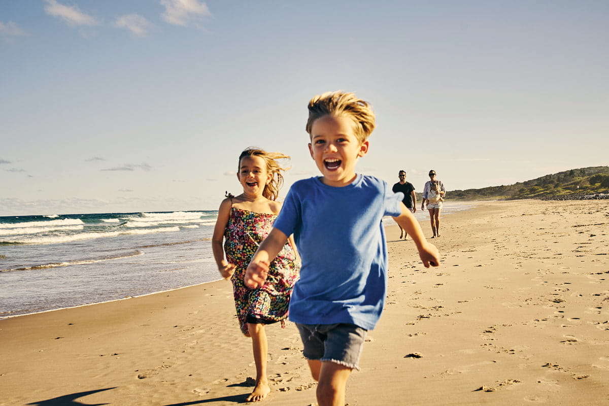 two little kids running on beach with parents in background