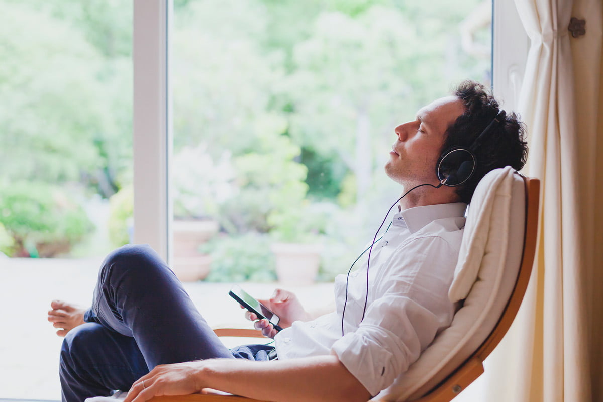man in modern bright interior in chair barefoot, eyes closed, wearing headphones