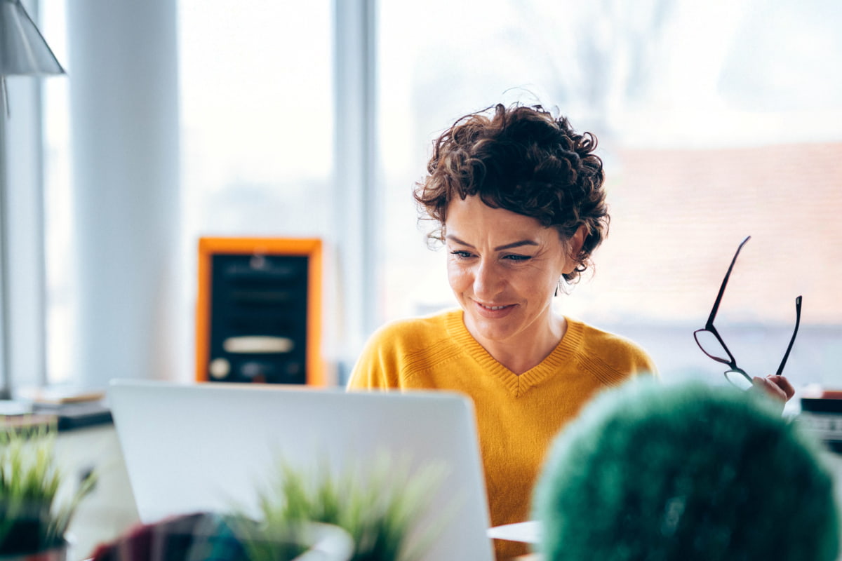 business woman working on laptop wearing orange sweater holding glasses