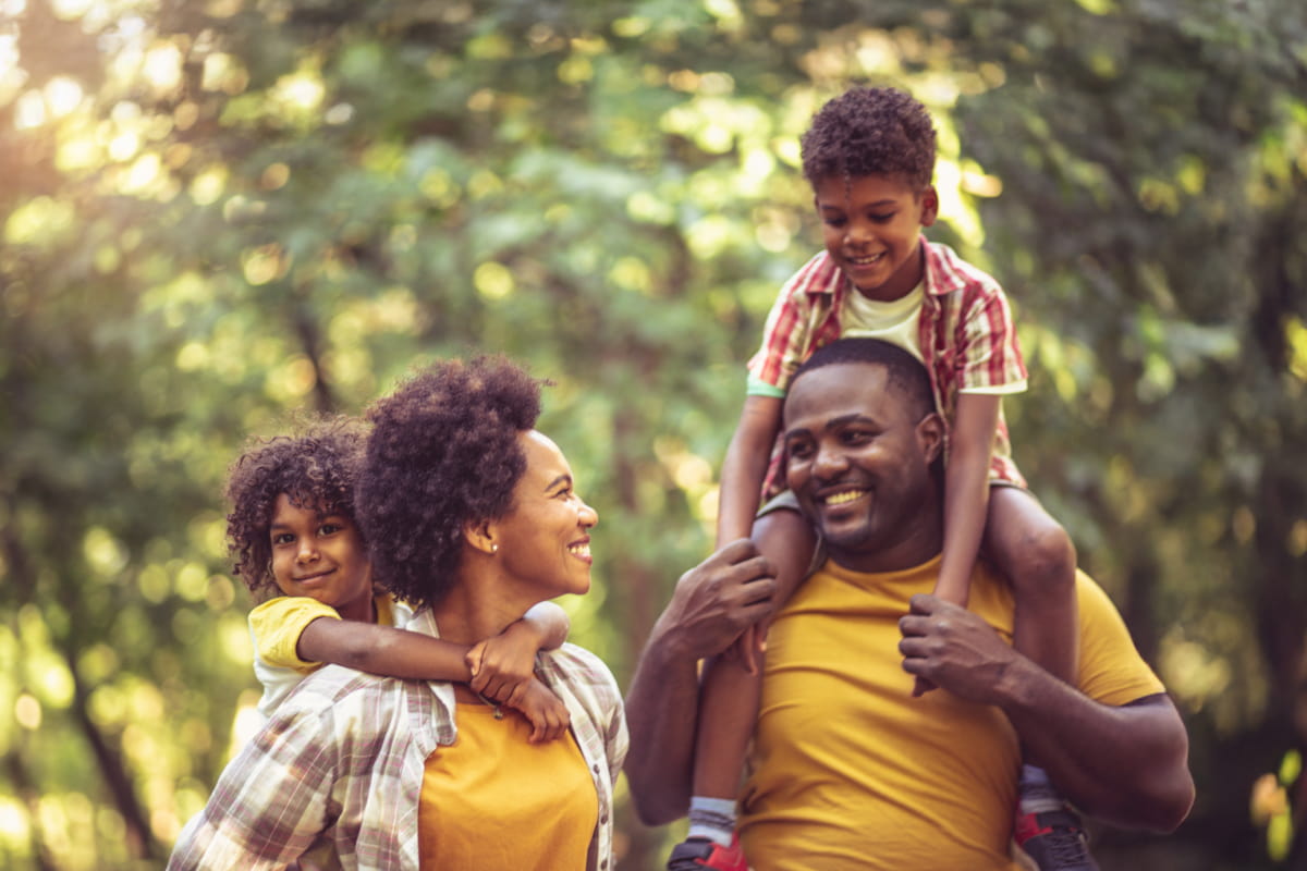 African American family having fun outdoors carrying son and daughter on shoulders